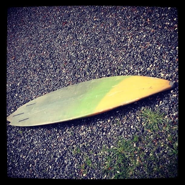 An early Tony Logosz shape lying on gravel — a single-fin board faded green and yellow